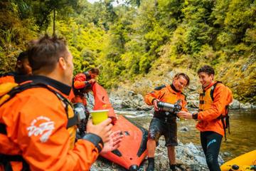 People on a rafting trip take a break to drink coffee on the riverbank.