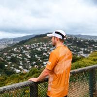 A runner wearing an orange teeshirt and white cap looks out over the hills of Wellington.