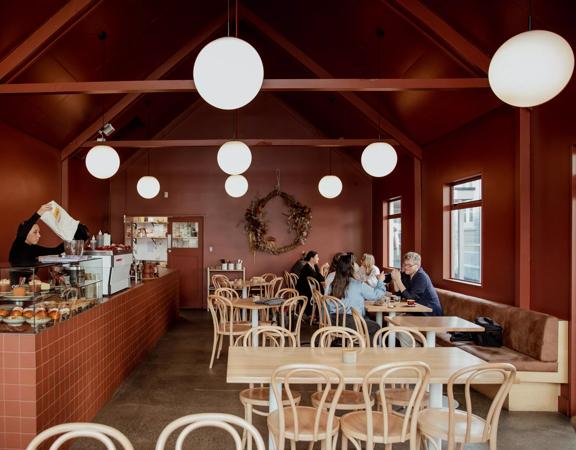 Wide view looking into the interior of August Eatery in Wellington. With people sitting at tables talking and the barista filling the coffee beans.