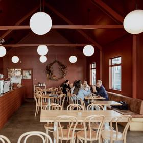 Wide view looking into the interior of August Eatery in Wellington. With people sitting at tables talking and the barista filling the coffee beans.