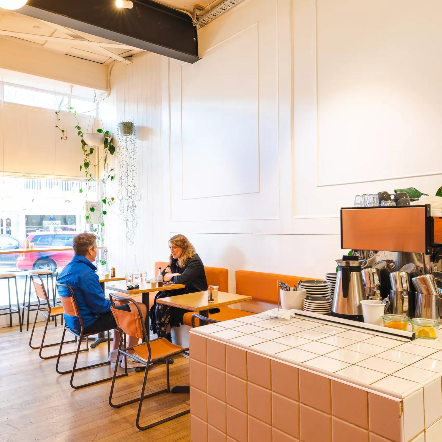 Two friends sit across from one another at a small table inside Fred's, a sandwich shop on Cuba Street in Wellington.