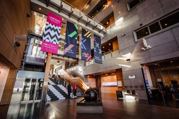 The lobby of Te Papa Museum. High ceilings, large posters and an elevator can been seen.