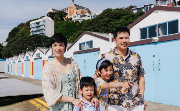 Two adults and two children are standing in front of the colourful boat sheds at Oriental Bay in Wellington.