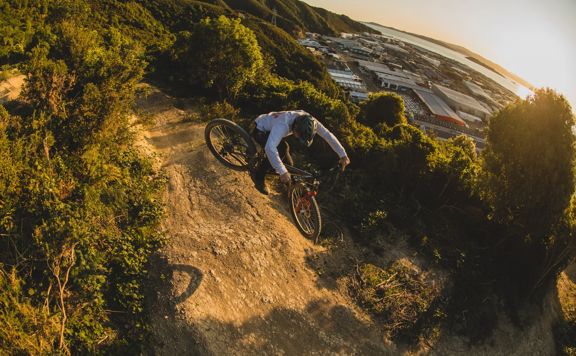 A mountain biker jumps on a dirt track amongst trees on Churnobull trail in Wainuiomata Park.
