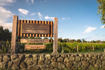 A rusted corregated iron sign outside Ata Rangi vineyard in the Wairarapa region. The green vineyard is behind it.