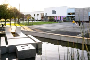 Family walking towards thre Dowse Museum. There is a large statue of a square man floating in the water.