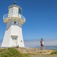 2 poeple standing underneath the Pencarrow lighthouse, with the ocean int eh background.