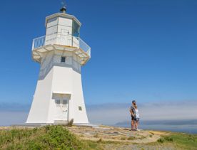 2 poeple standing underneath the Pencarrow lighthouse, with the ocean int eh background.