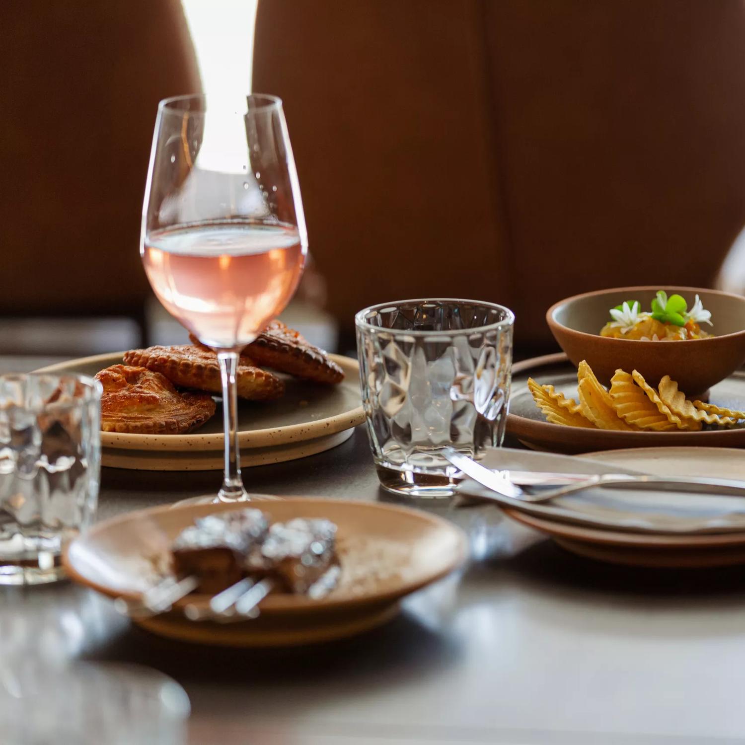 A table laden with plates of food with a glass of rosé wine and water glasses.