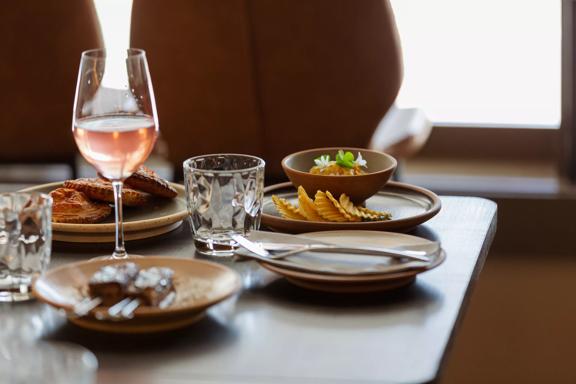 A table laden with plates of food with a glass of rosé wine and water glasses.