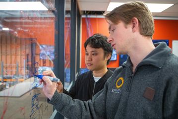 Two OpenStar employees draw diagrams on a dry-erase board.