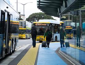 Two people walk towards the Airport Express bus while stopped at Wellington Railway Station.