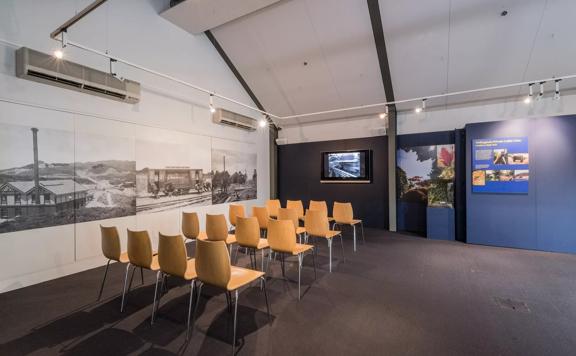 Wide look at a small group of chairs in a room at the Cable Car Museum lined up facing a television screen with a historic video playing.