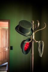 A wooden coat rack with three hats on the hooks inside a green-walled room at the Nairn Street Cottage in Wellington.