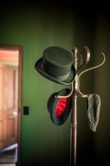A wooden coat rack with three hats on the hooks inside a green-walled room at the Nairn Street Cottage in Wellington.