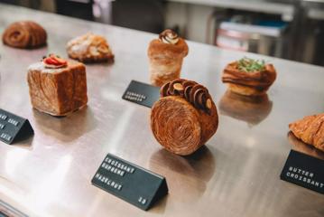 Decadent pastries of different shapes sit on a metal bench with black name cards in front.