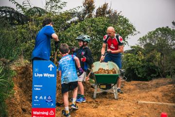 Two adults and two children use a shovel and a wheel barrel to build a trail.