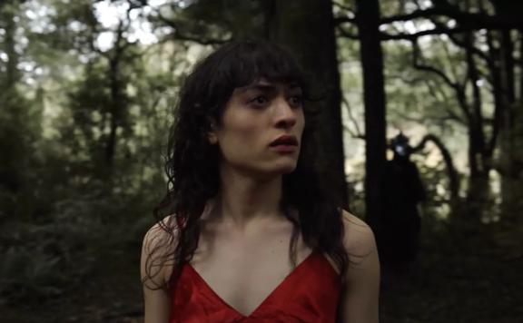 A still from Awa Puna's short film 'Tūī'. A young woman (Puna) standing in a dark forest. 