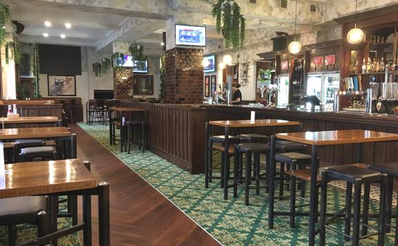 Interior of The Bridge bar. There are several high tables with bar stools and the bar lines one wall.