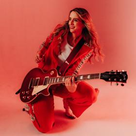 Kaylee Bell crouching down while holding an electric guitar.