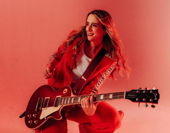 Kaylee Bell crouching down while holding an electric guitar.