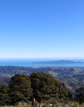 A scenic view of mountain ranges, the ocean and a small island under the clear blue sky.