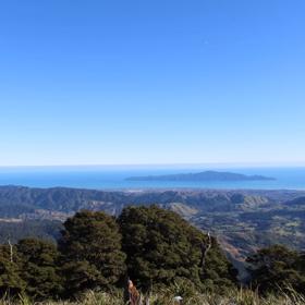 A scenic view of mountain ranges, the ocean and a small island under the clear blue sky.