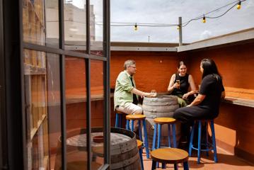 Outside seating area of Ascot, with barrel tables and high bar chairs. Orange painted brick walls and rustic decorations occupy the background.