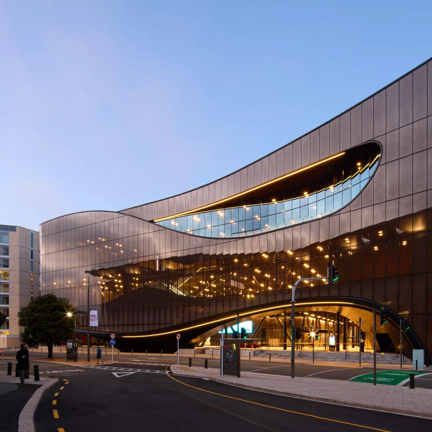 The exterior of Tākina at sunset, with orange lights shining through the glass.