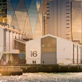 Looking across the waterfront at Shed 6, a building on the Queens Whard with large doors and the Shed 6 sign.
