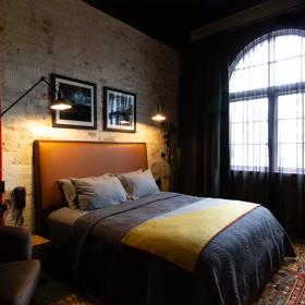 A moody and dark hotel room inside The Intrepid Hotel on Ghuznee Street. A beige brick wall is surrounded by rustic accents and a double bed.