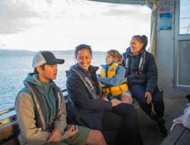 Four people sit on a boat smiling wearing life vests. 