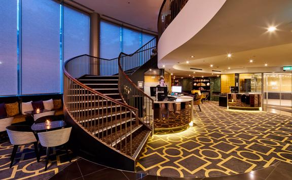 Inside the lobby at the Bolton Hotel in Wellington with a curved staircase and a worker standing behind the front desk. 
