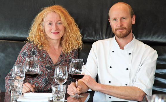 Capitol restaurant co-owners Kate Hutchison and husband Tom Hutchison (chef), sitting at a small table with a glass of wine.