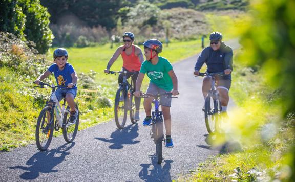 Four cyclists are riding on the path in Queen Elizabeth Regional Park, located in Paraparaumu, New Zealand.