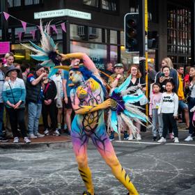 A CubaDupa performer wearing bright body paint and holding feathers dances for the crowd surrounding at CubaDupa 2021.