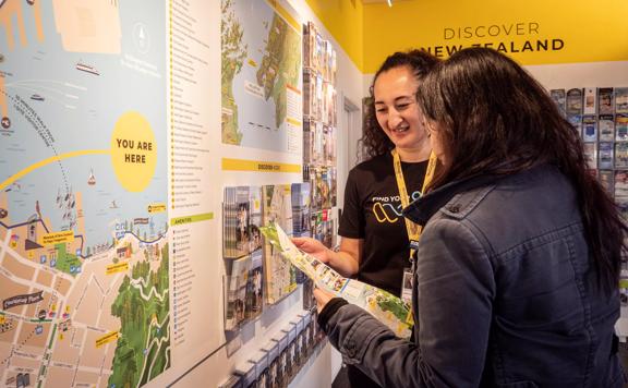 A staff member at Wellington's iSite, a tourism information centre, helps a tourist look at a map.