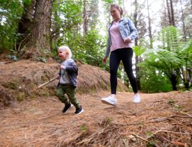 Parent and child carrying a stick walking through the pine needle covered Spicer Link Track in Porirua.