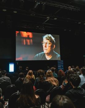 Delegates at New Zealand Game Developers Conference watch a video playing on a projector.