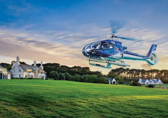 The Wellington Helicopter flying low on a field with houses in the background during sunset.