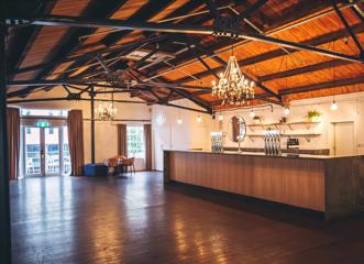 Interior of large, empty conference room, with rustic orange roof and hardwood floors. A bar sits to the right of the image lit by a chandelier.