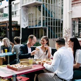 The patio at Golding's bar located in Te Aro in Wellington, with four tables, twelve stools and eight people sitting enjoying beer and pizza. 