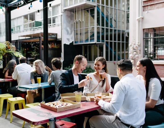 The patio at Golding's bar located in Te Aro in Wellington, with four tables, twelve stools and eight people sitting enjoying beer and pizza. 