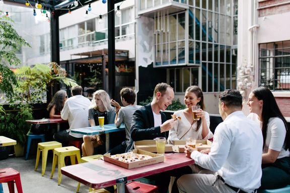 The patio at Golding's bar located in Te Aro in Wellington, with four tables, twelve stools and eight people sitting enjoying beer and pizza.