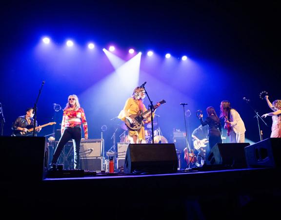 Atomic! 2.0, an all-female tribute band, performs on stage under purple spotlights.