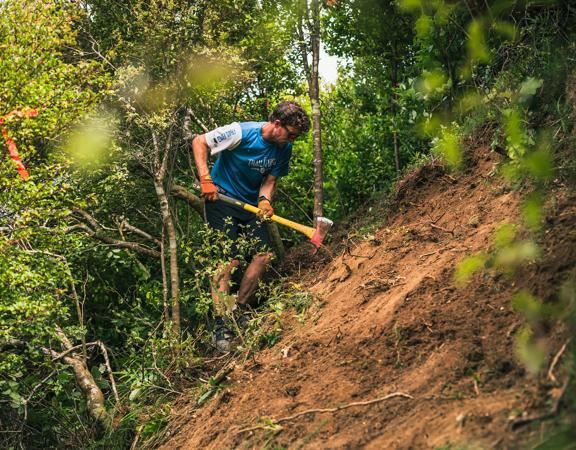 A person using an axe to build a trail in the forest.