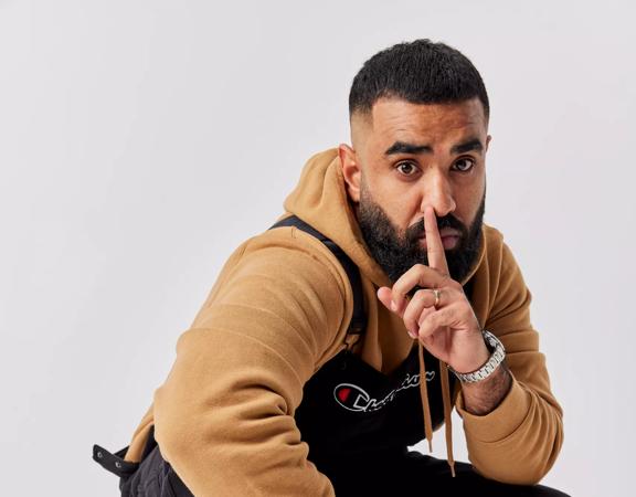 New Zealand comedian, Pax Assadi, posing with his index finger over his lips for to promote his stand-up comedy show 'Secrets'.