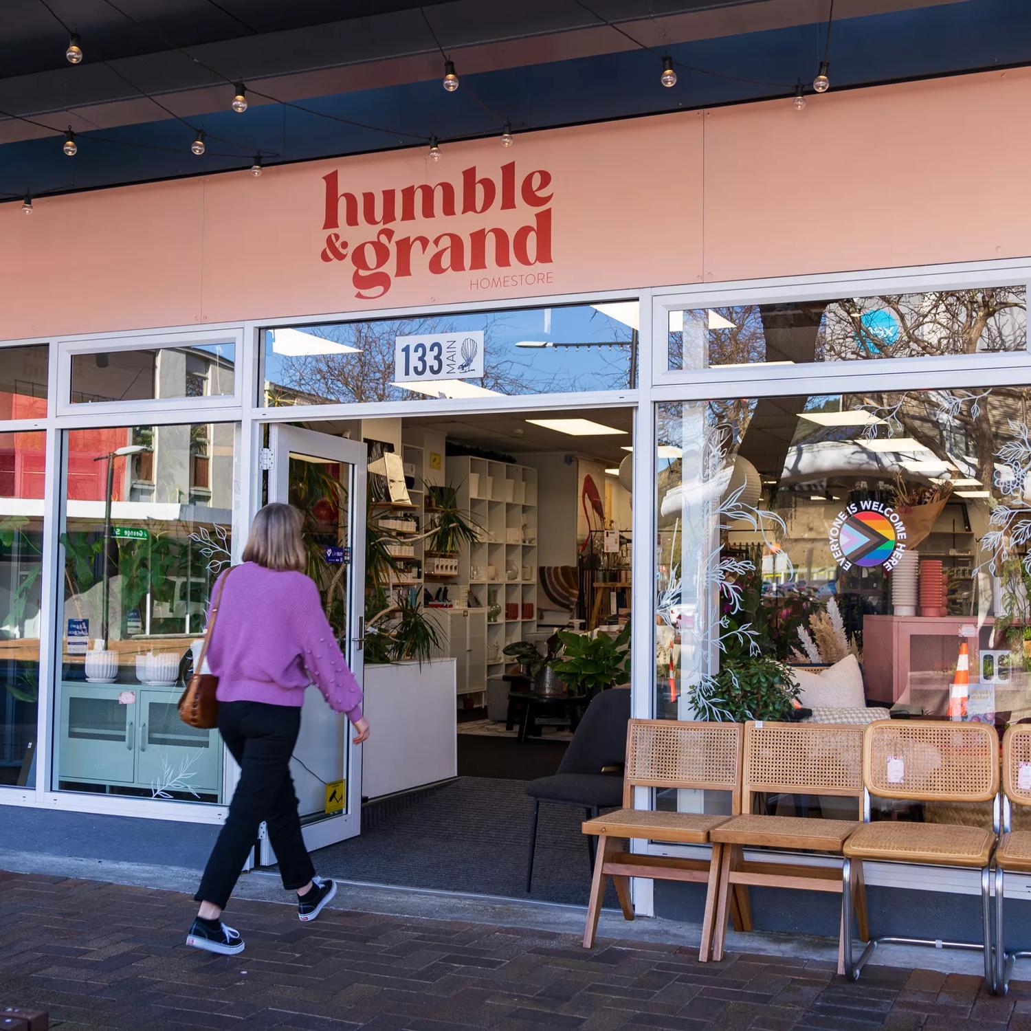 Person walking into Humble & Grand, with its peachy pink exterior and chairs sat outside.