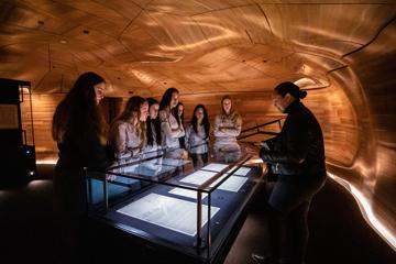 Students crowd around an exhibit on a visit to The National Library of New Zealand, Te puna Mātauranga o Aotearoa. Anna Tiaki facilitating tour of He Tohu.