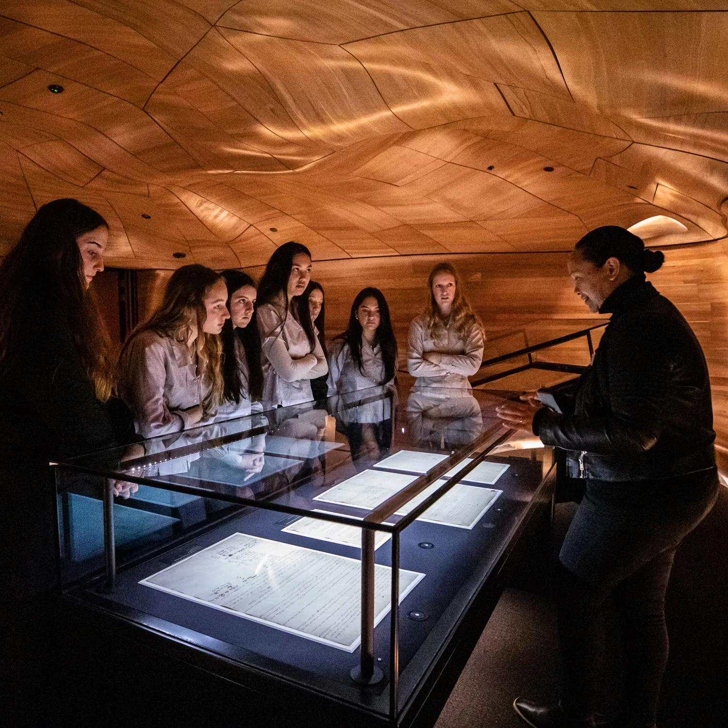 Students crowd around an exhibit on a visit to The National Library of New Zealand, Te puna Mātauranga o Aotearoa. Anna Tiaki facilitating tour of He Tohu.